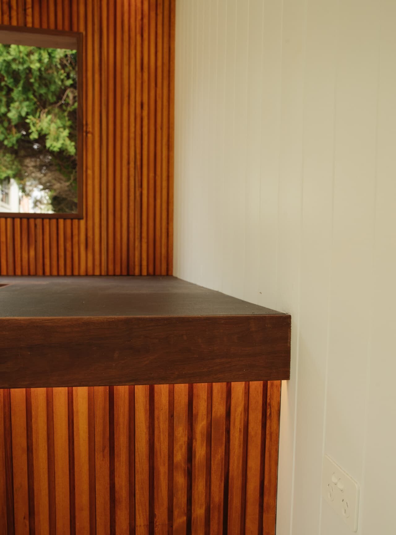 Timber batten bench with a dark concrete top and a hardwood-framed window