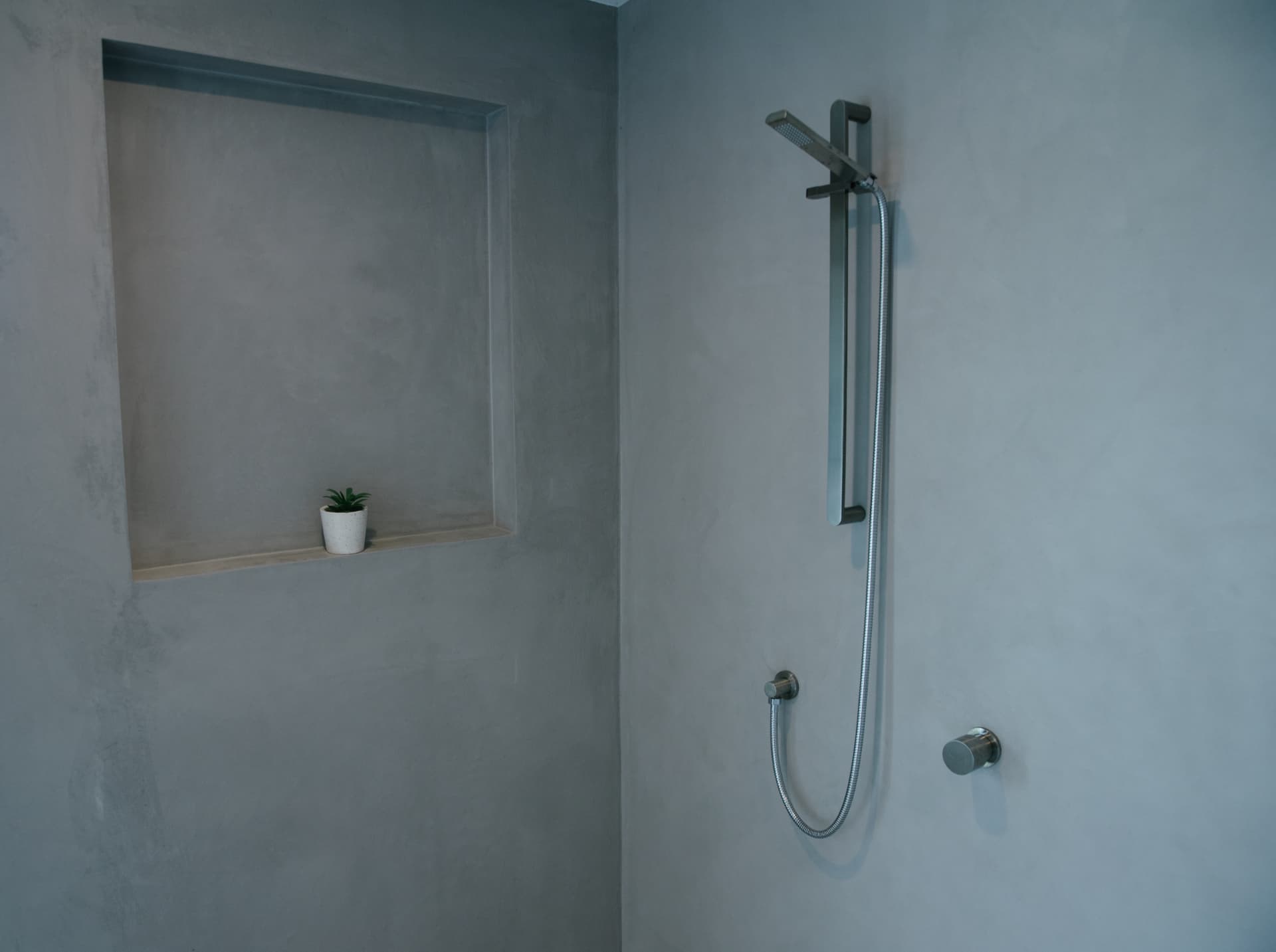 Stainless shower rail and mixer against a soft grey plaster corner